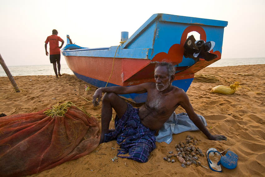 Elderly fishermen resting after counting his catch of shells, Kochuveli, Kerala